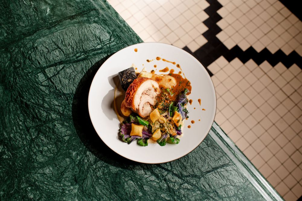 A plated dish on a marble surface with a tiled background showcasing modern restaurant cuisine with garnishes and sauces.