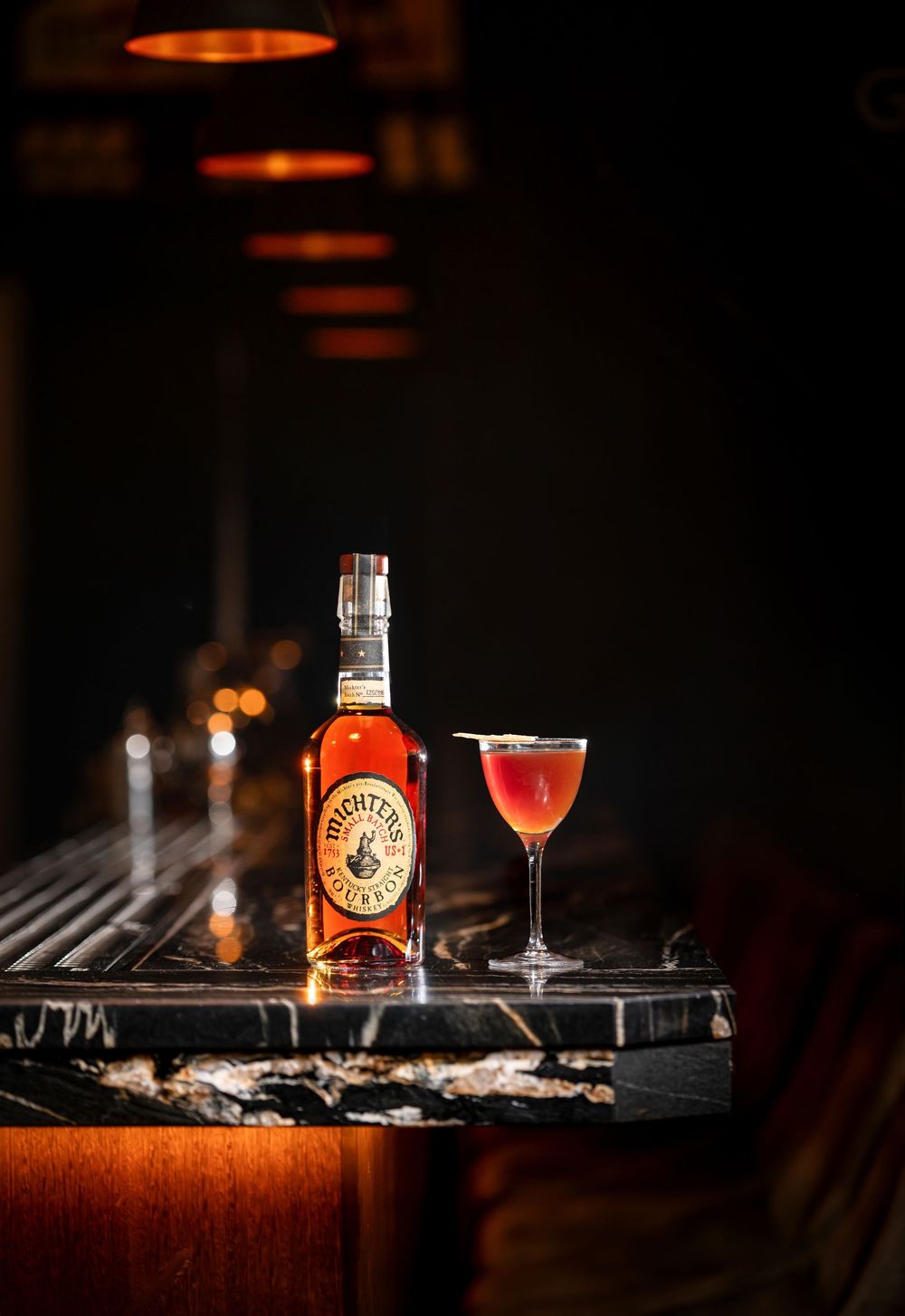 Bottle and cocktail glass arranged on dark wooden surface with moody lighting.