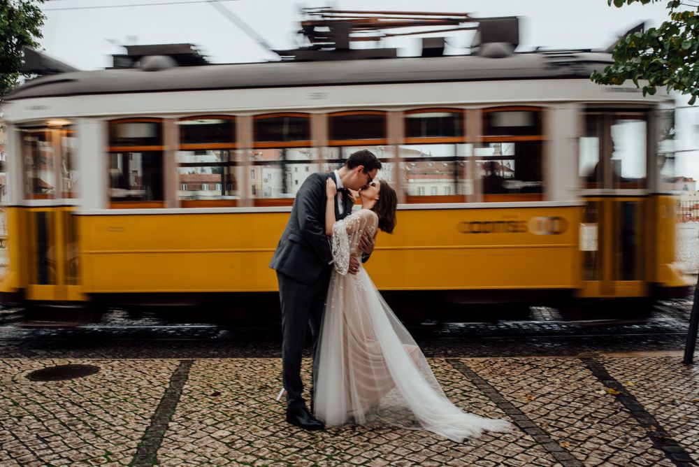 Bride and groom kissing with a blurred yellow tram in movement in the streets of Lisbon.
