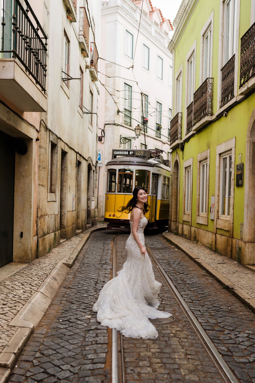 A bride running after a yellow tram in a narrow street of Lisbon.