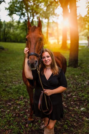 A brown horse stands with someone in a black dress in a wooded area during golden hour sunset. Janesville, WI
Brodhead, WI