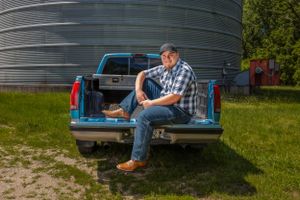 Person in plaid shirt sitting casually in the bed of a blue pickup truck near a grain silo.
Janesville, WI
Brodhead, WI
