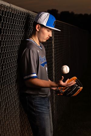 Baseball player in dark uniform practicing pitching technique against chain link fence in sequence of motions.