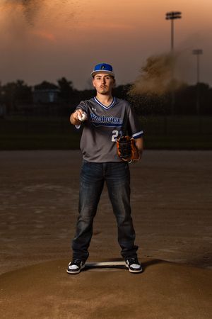 A baseball player in a blue jersey stands in a dramatic pose on a dirt field at sunset.