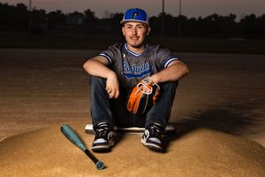 Baseball player sitting in dugout wearing uniform and cap while holding bat during game.