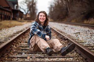 Someone sits casually on railroad tracks wearing a plaid flannel shirt and khaki pants on a cloudy autumn day.
Janesville, WI
Brodhead, WI