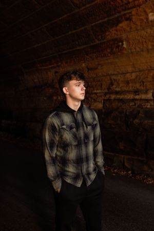 Person in plaid flannel shirt and dark pants standing in moody dark tunnel with textured stone walls. Janesville, WI
Brodhead, WI