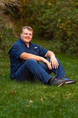 A person in navy blue clothing relaxes on green grass in a casual outdoor portrait series.