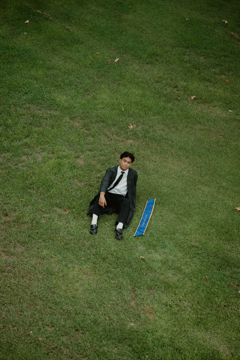 Someone in a dark suit lies on green grass next to a blue ruler on a sloping lawn.