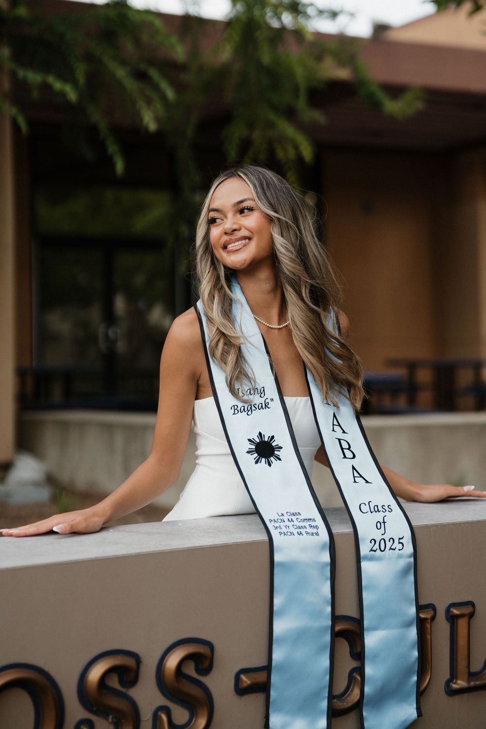 A graduation photo series showing someone in white posing against a railing with ombre decorations.