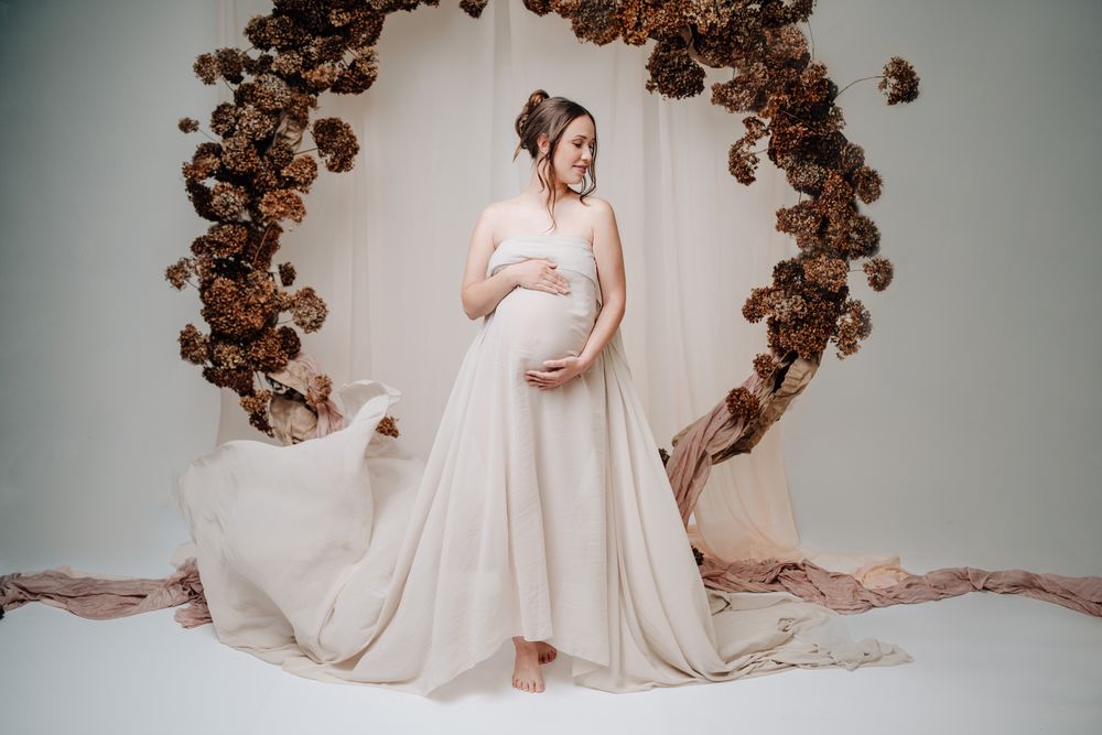 A maternity portrait featuring a flowing dress and decorative brown floral arch backdrop.Babybauch  Fotografie Hessen