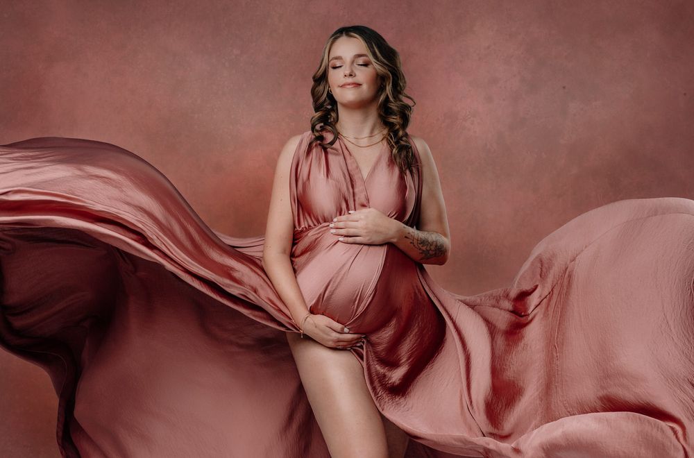 Flowy pink silk maternity dress billows elegantly in studio portrait with mauve backdrop.Babybauch  Fotografie Hessen Wetterau
