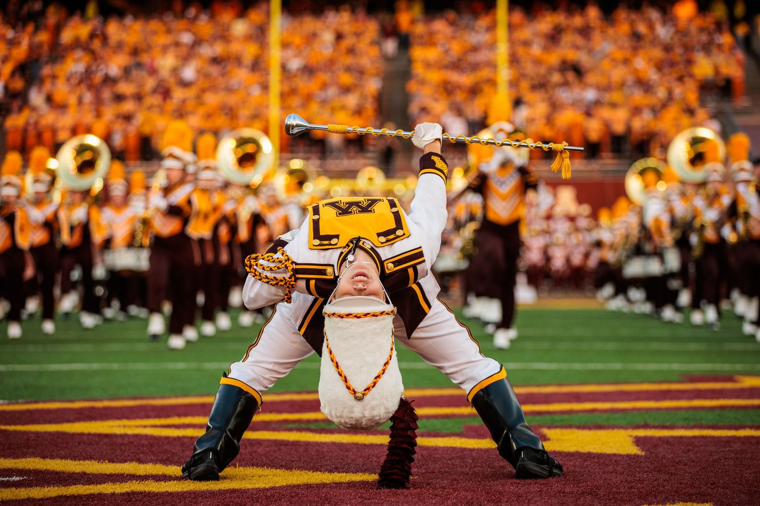 Drum major performing a back bend while looking into camera. Band mates high stepping to camera.