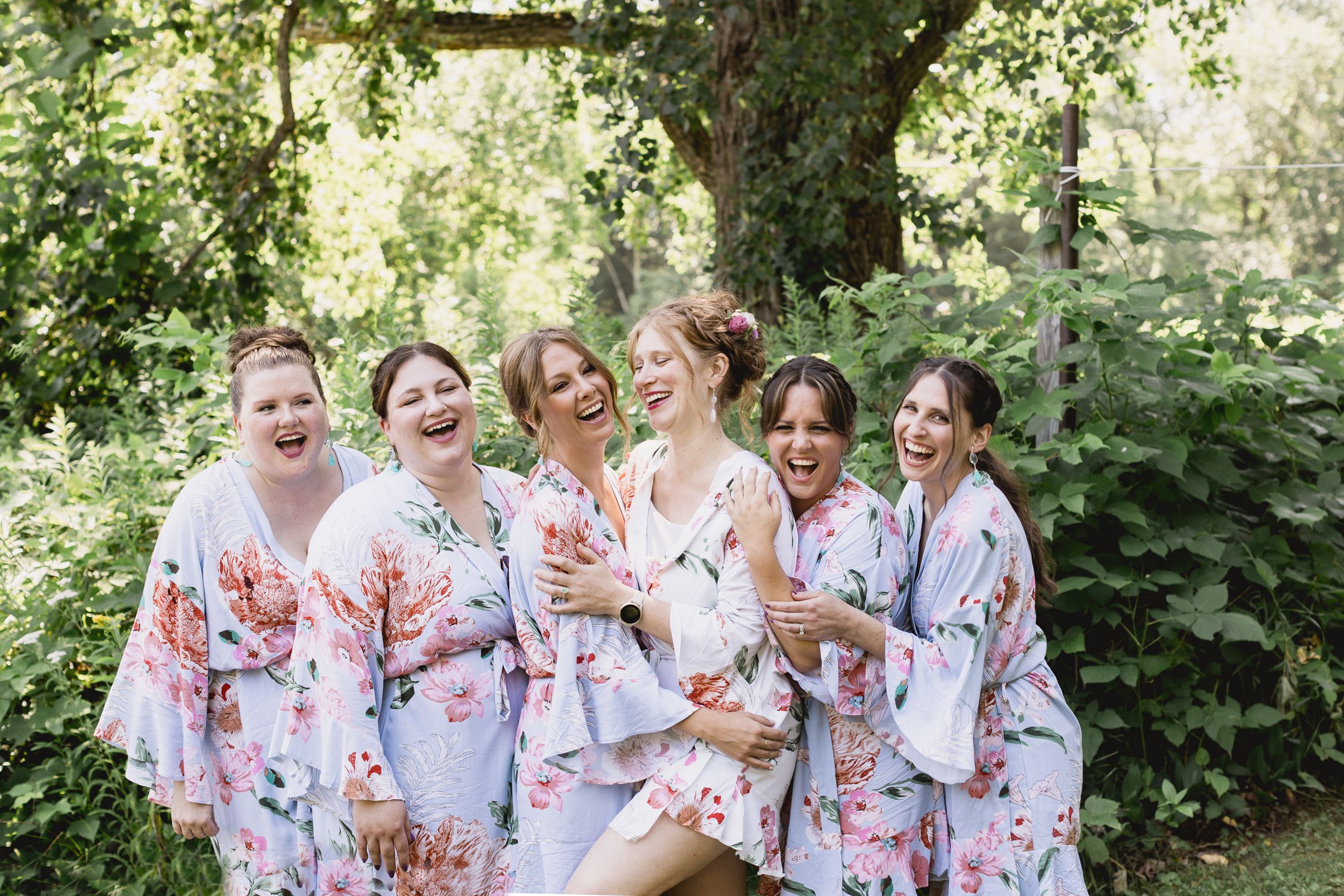 Group wearing matching floral robes laughs together in outdoor garden setting during special celebration.