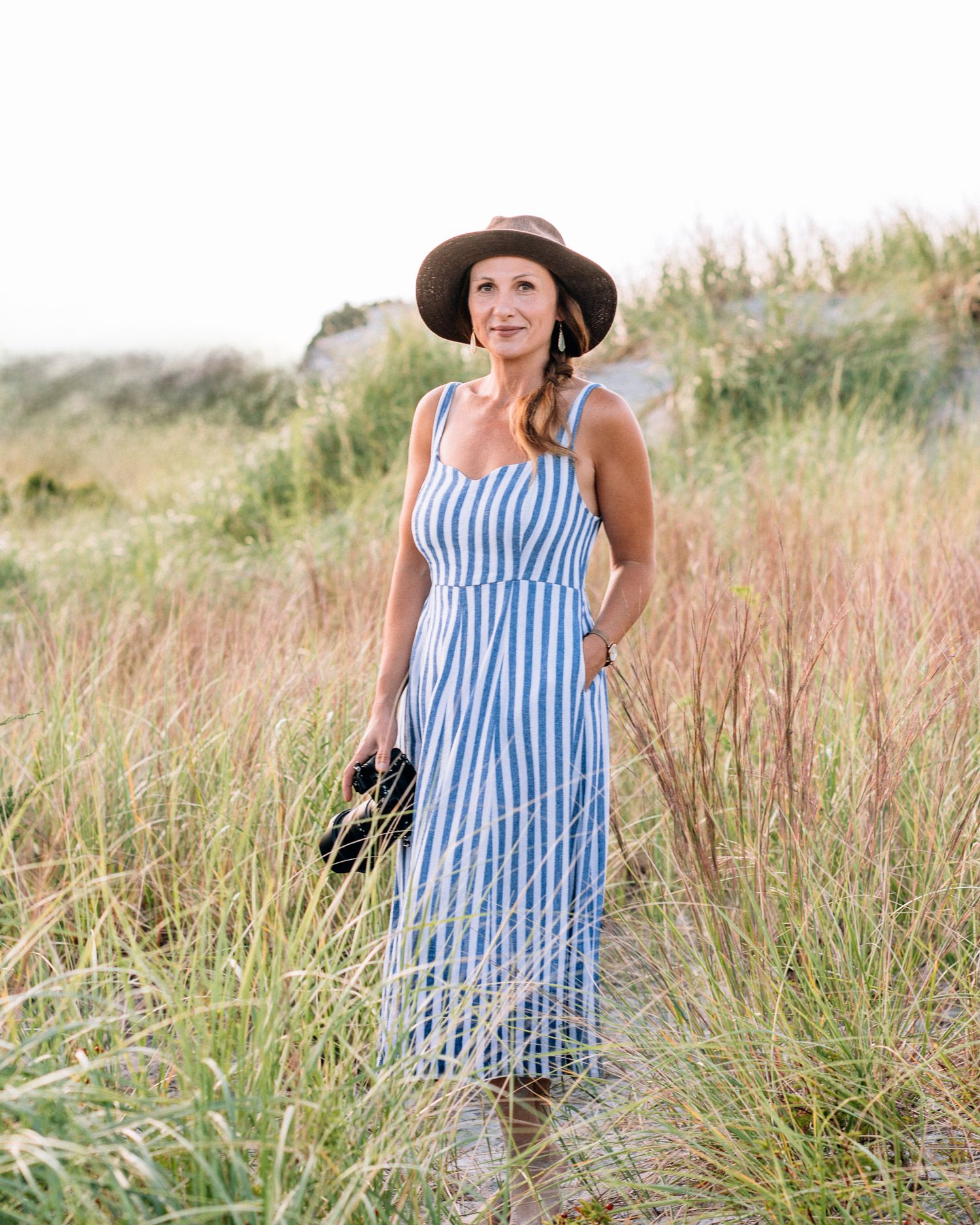 A photographer in a flowy dress and wide-brimmed hat captures photos in a sunlit forest.