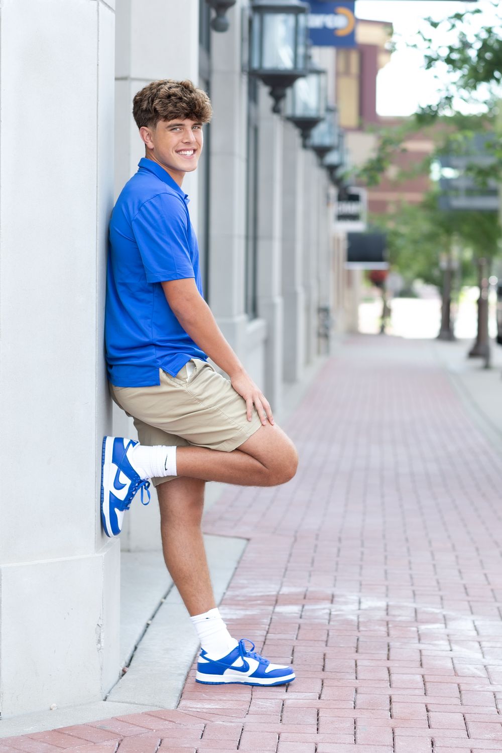 Athletic casual photoshoot with blue Nike polo and khaki shorts against white columns.