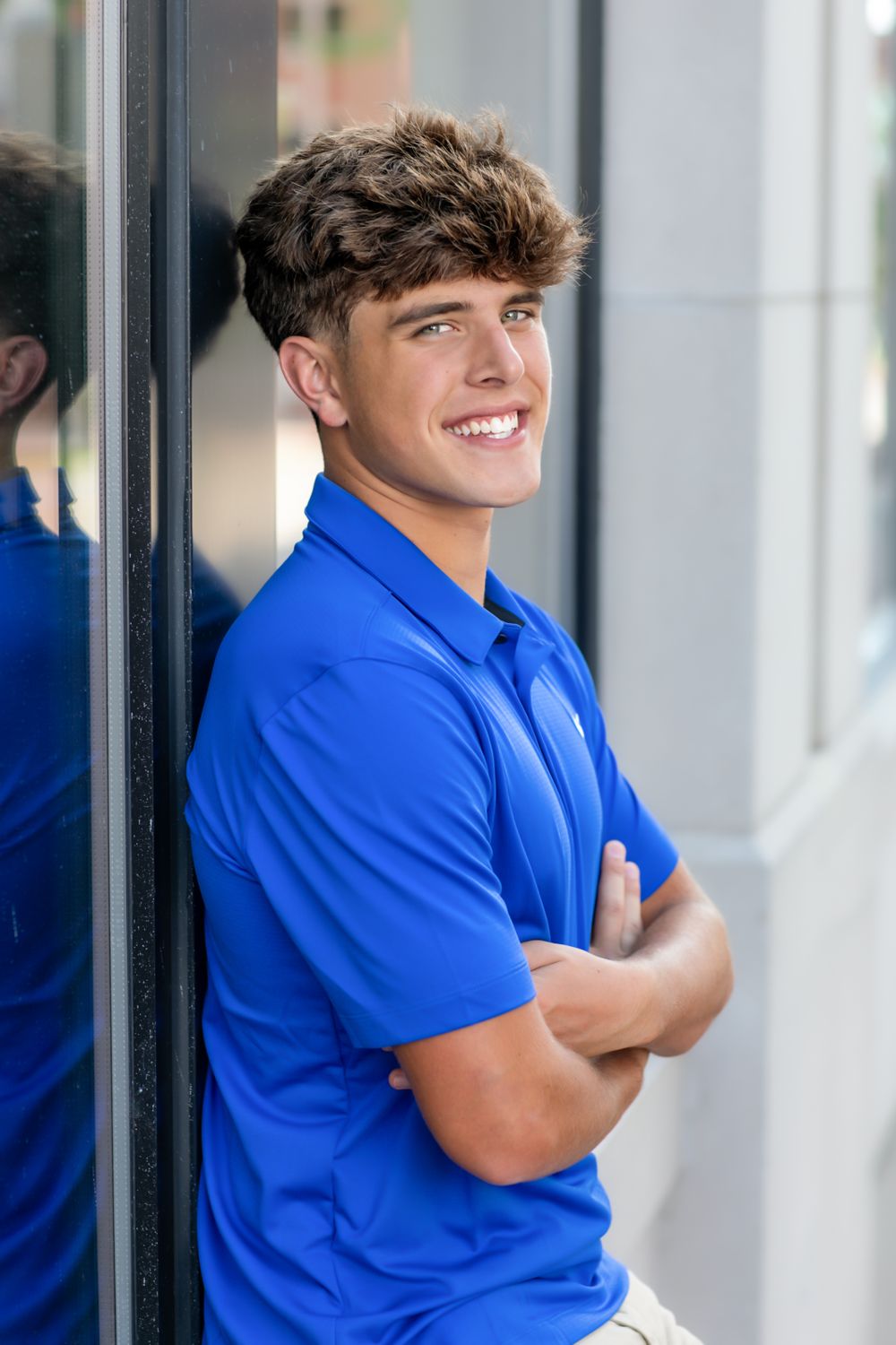 Student in bright blue polo shirt poses against white wall in casual portrait series.