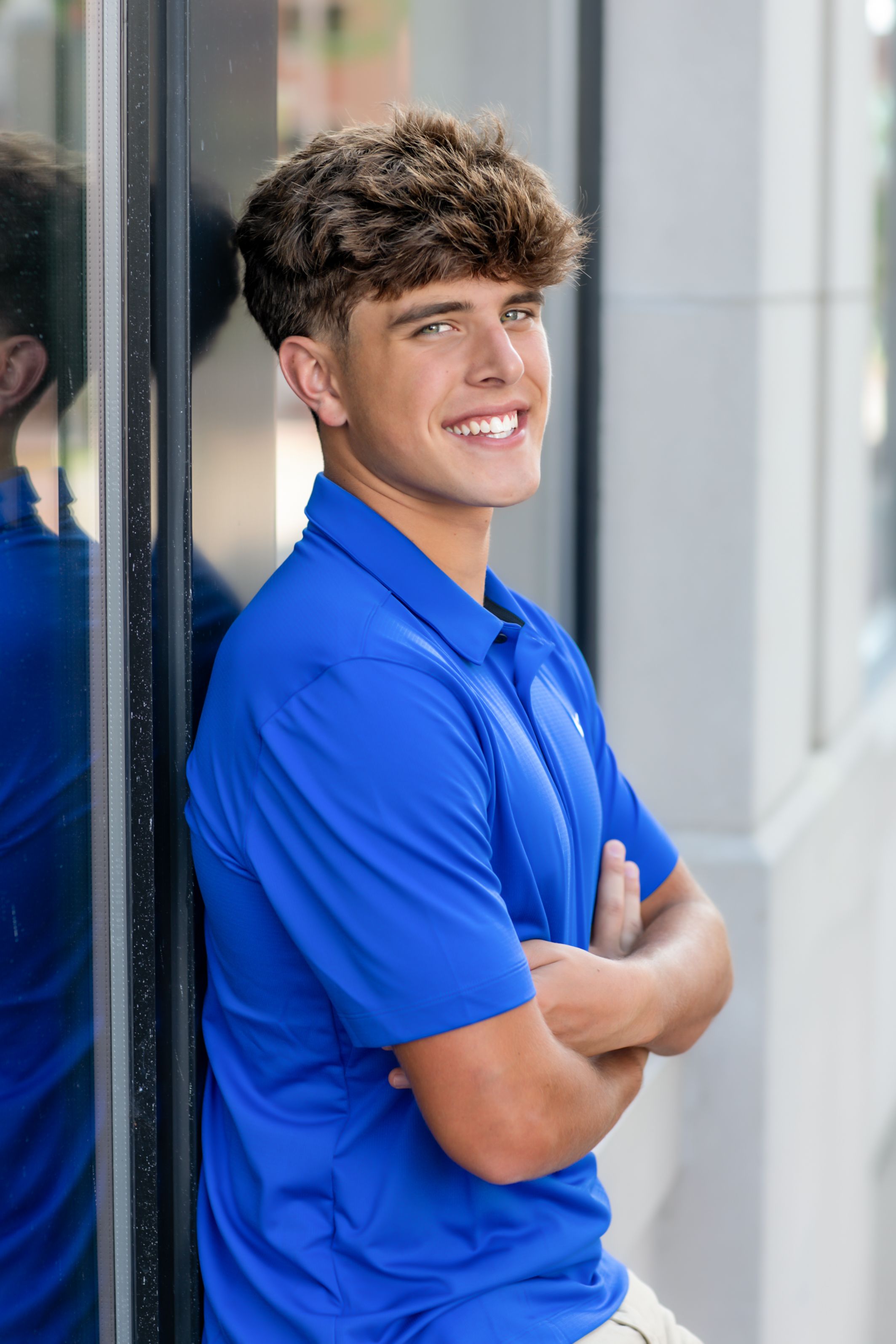 Student in bright blue polo shirt poses against white wall in casual portrait series.