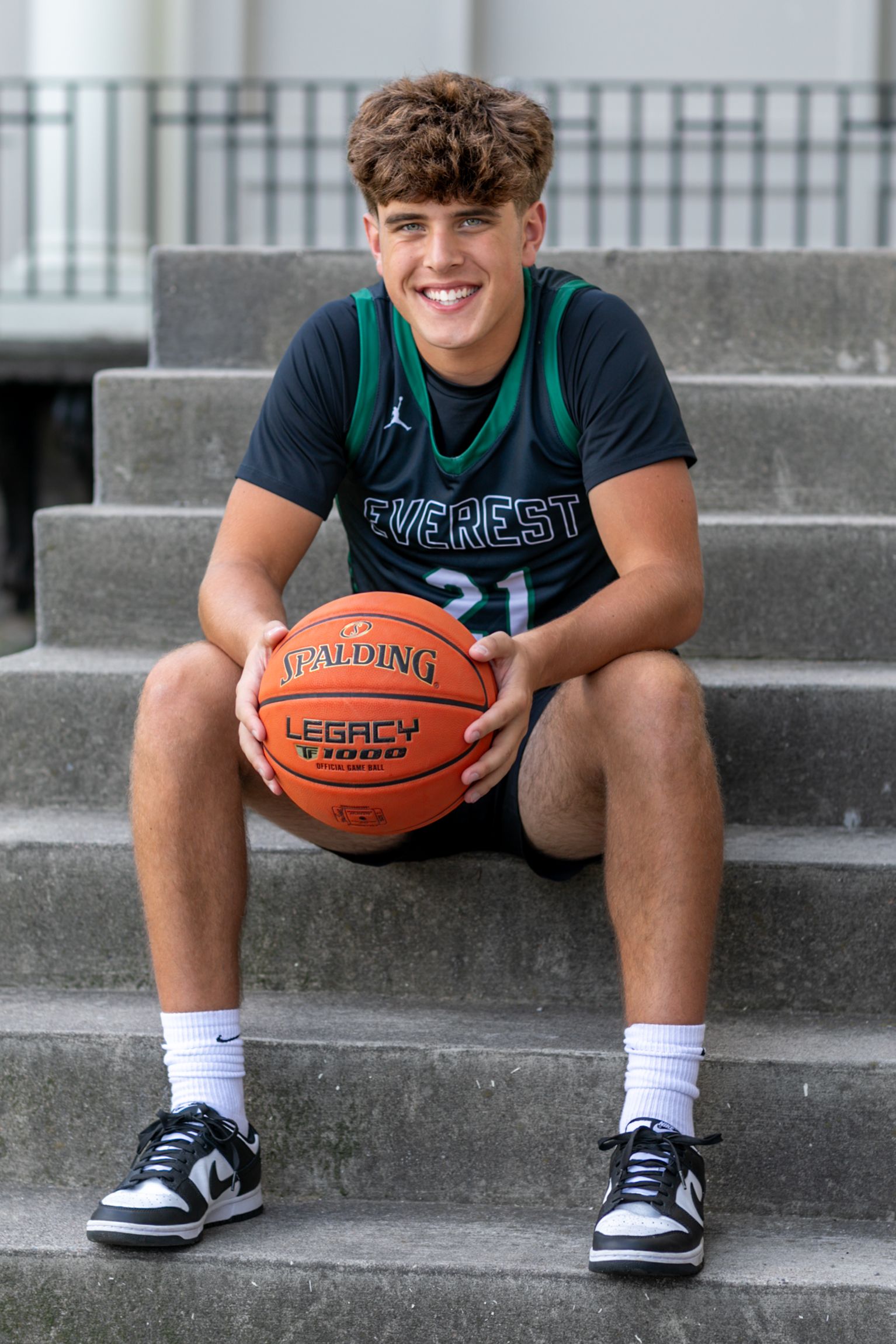 Student athlete sits on concrete steps holding a basketball in casual pose.