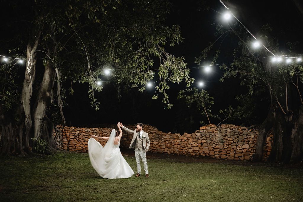 wedding Couple dancing under string lights at night in a garden with stone wall backdrop and trees overhead, intimate wedding at Intiem