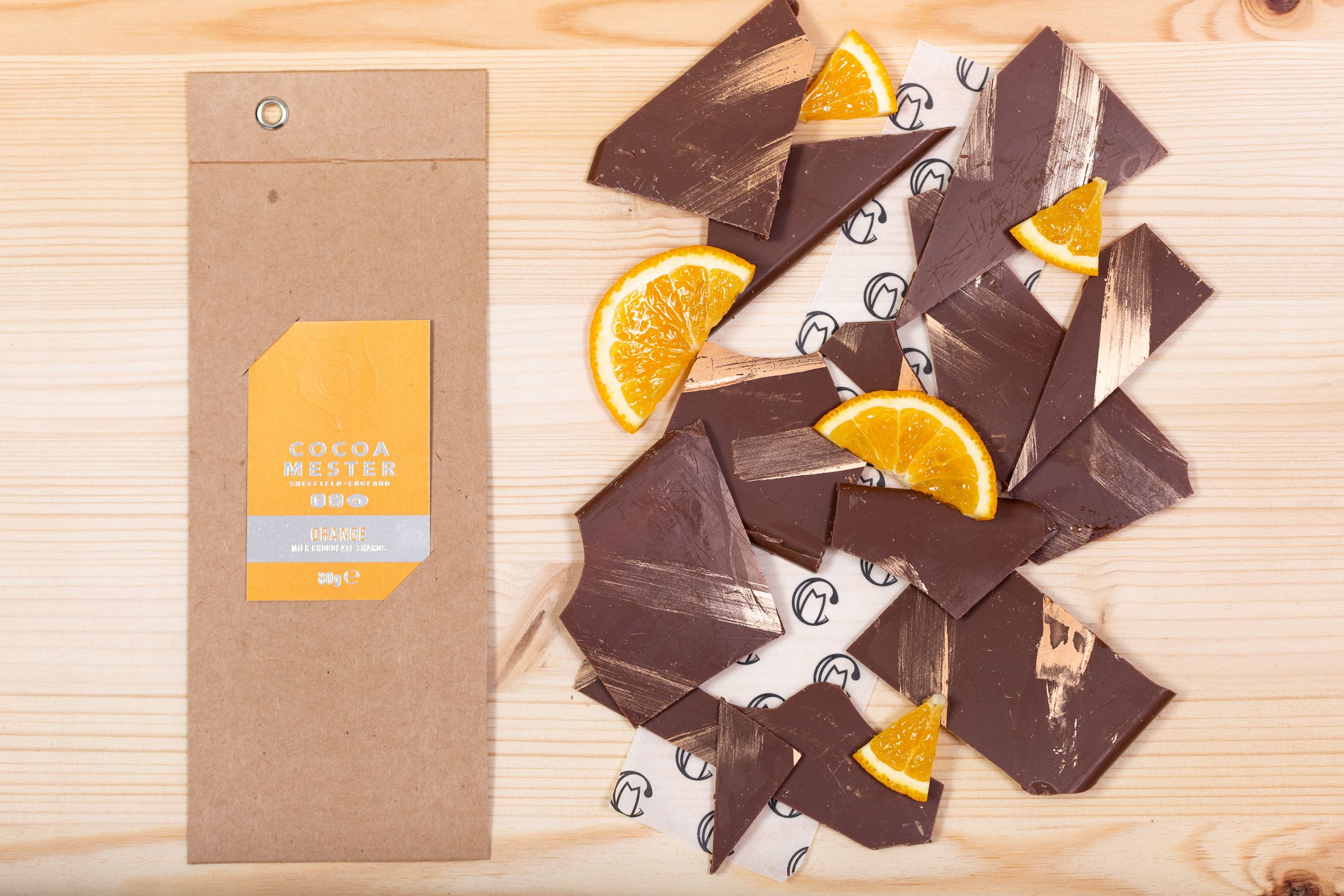 Artisanal dark chocolate bar broken into pieces with dried orange slices on wooden surface.