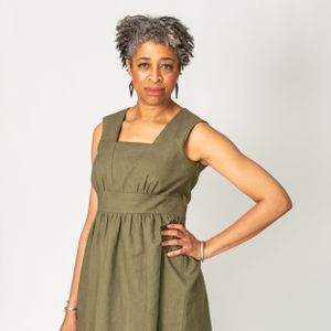 Woman wearing an olive green sleeveless dress poses against a white background.