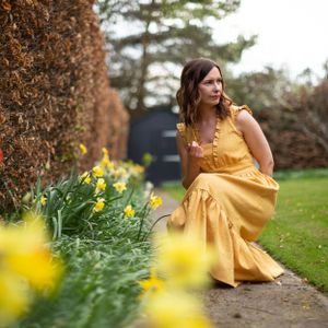 Yellow dress flowing in garden setting with daffodils and hedges.