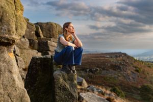 Person in casual wear sits contemplatively on rocky outcrop during sunset.