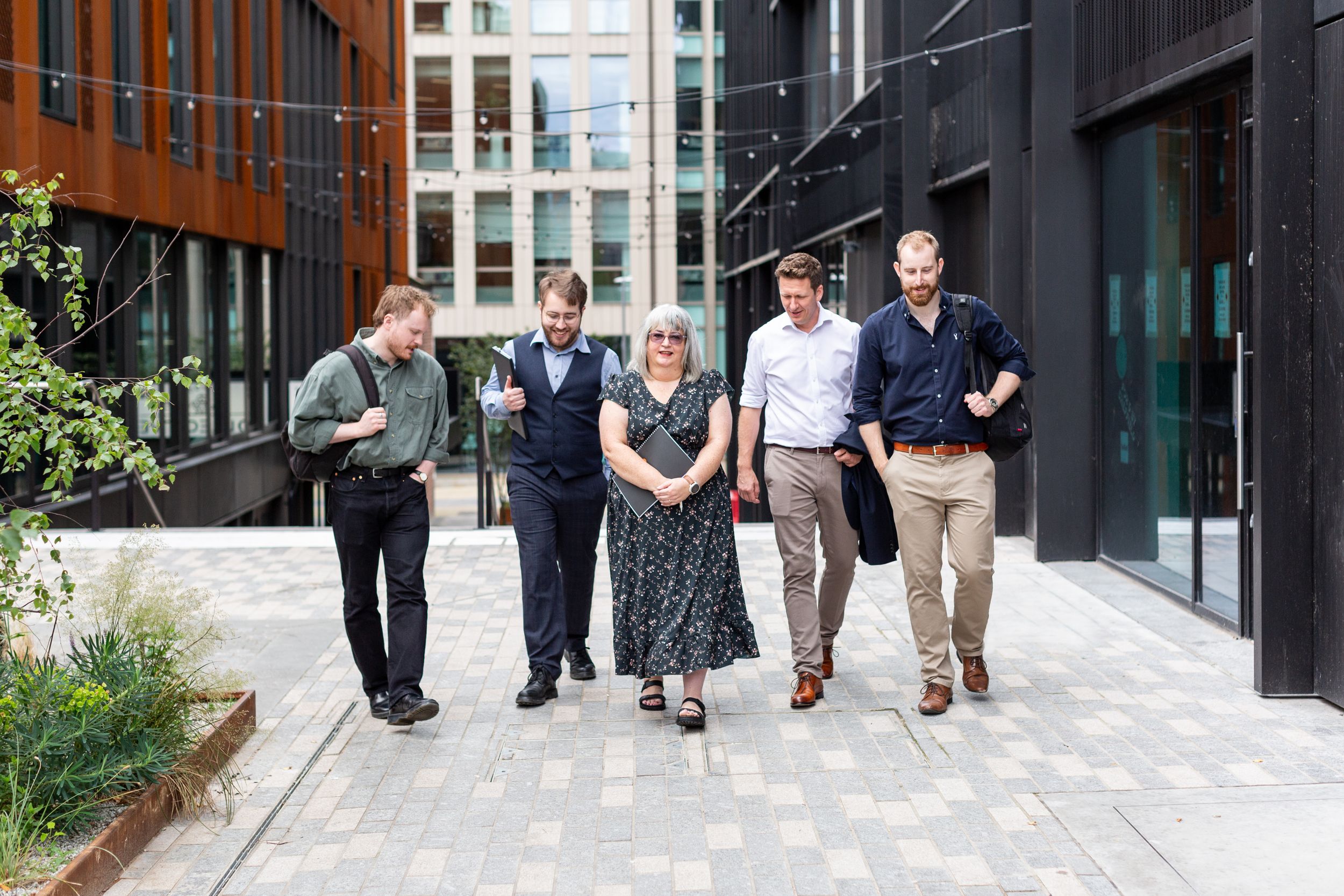 A group of professionals walking together on a modern office building walkway with landscaping.
