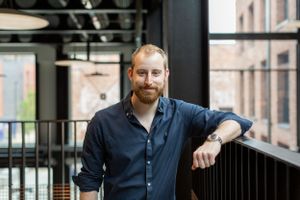A professional in a navy button-down shirt leaning on a railing in a modern office setting.
