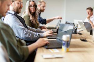 Team members working together at a conference table with laptops in a bright office.
