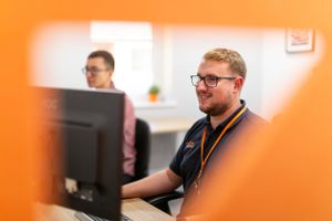 Professional working at computer desk in modern office with orange-tinted lighting.