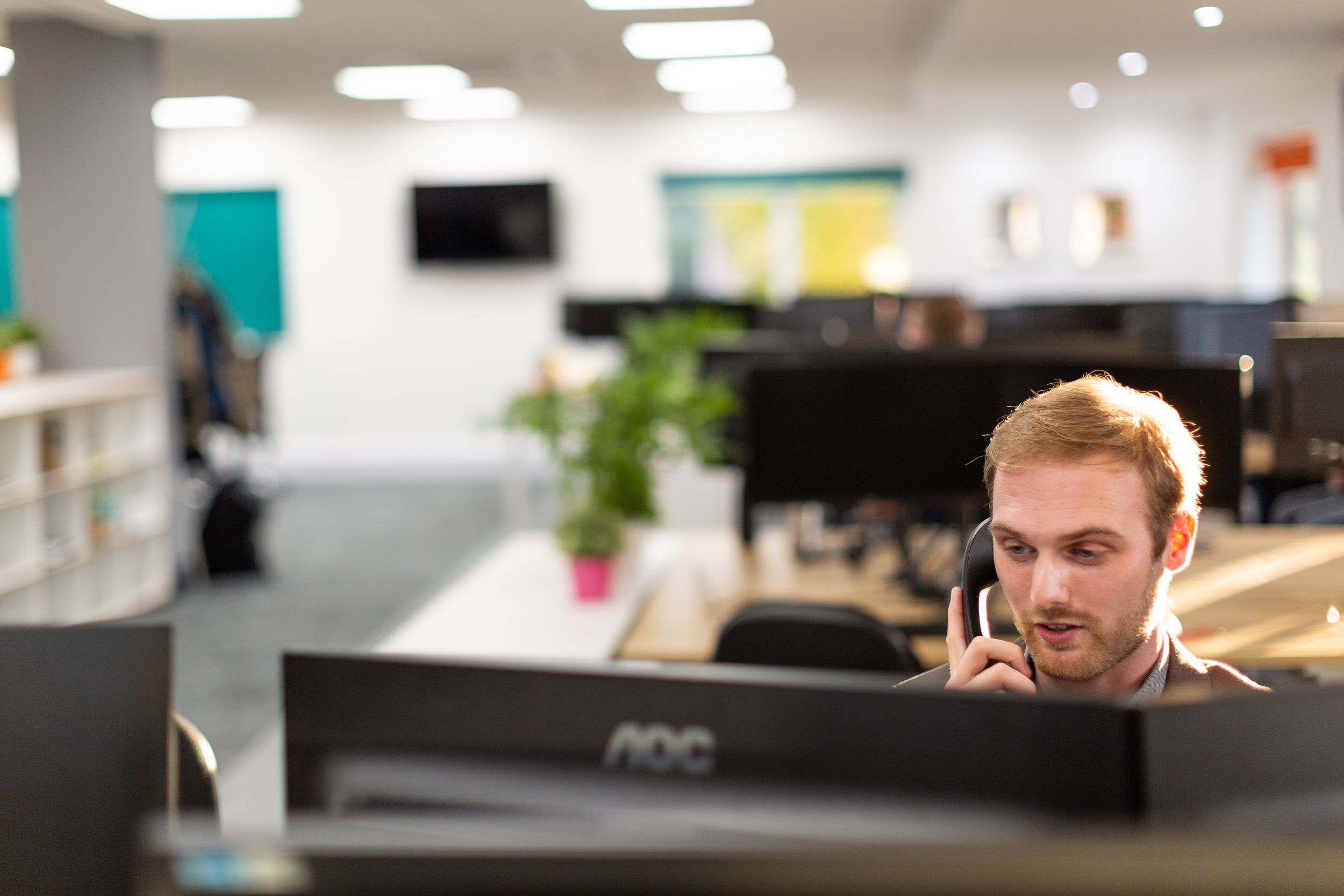 Professional taking a phone call at a modern desk workspace with computer monitors.