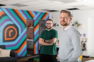 Two colleagues standing in an office with vibrant geometric wall art behind them.