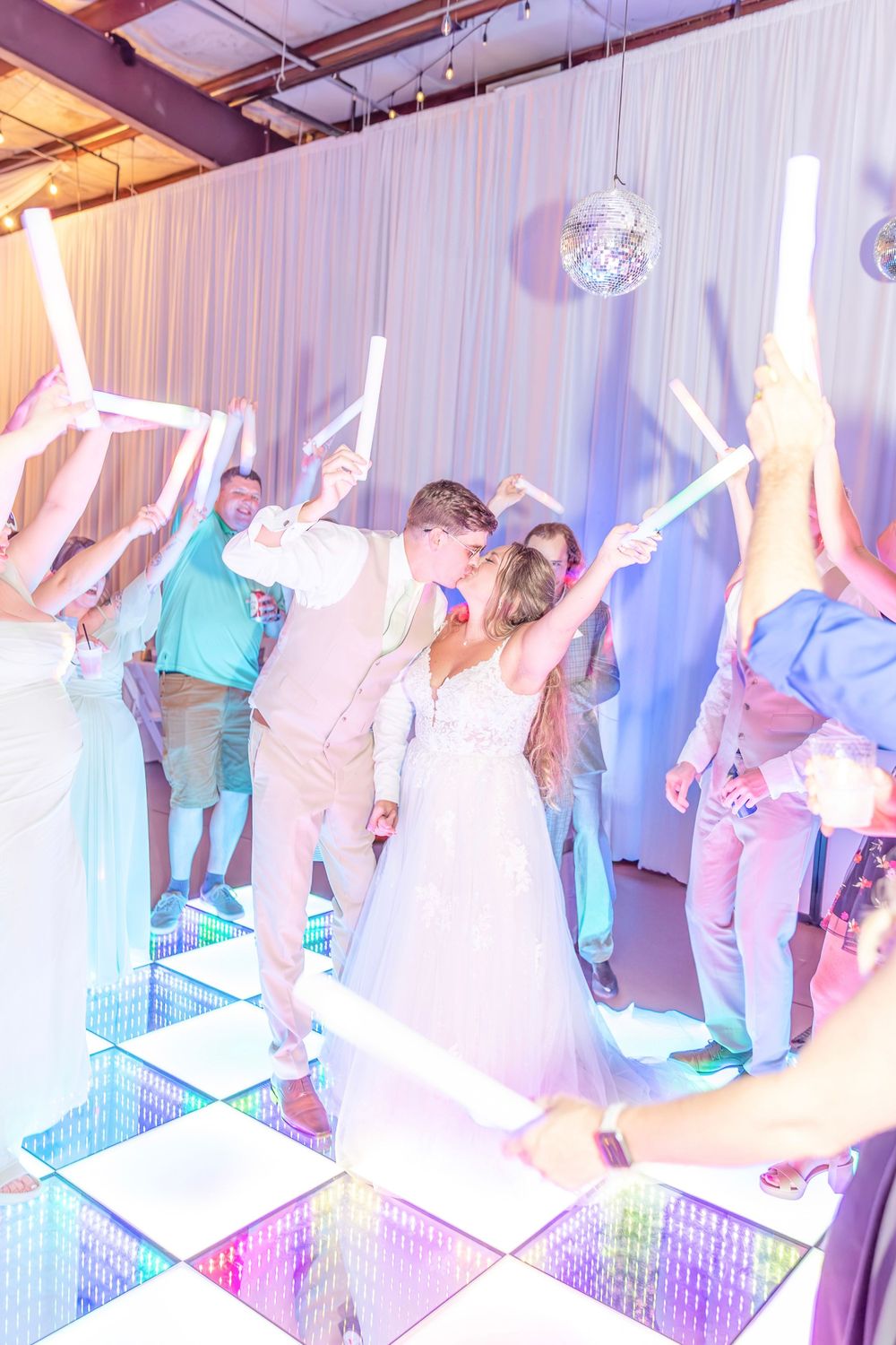 Wedding reception dance party with illuminated checkered floor and white draping.