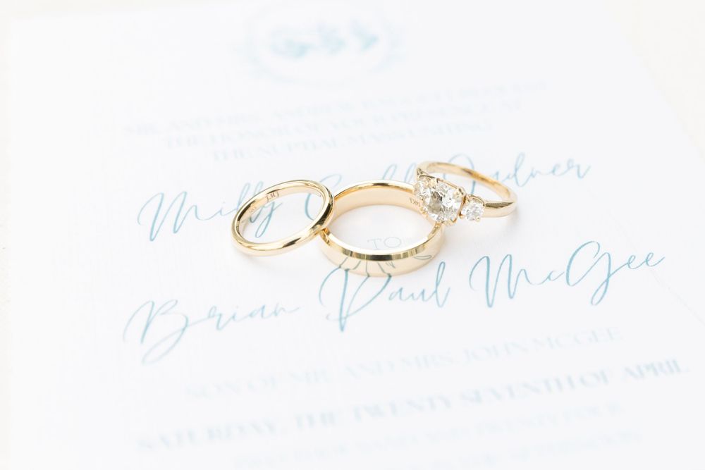 Three gold wedding rings arranged on light blue calligraphy paper.