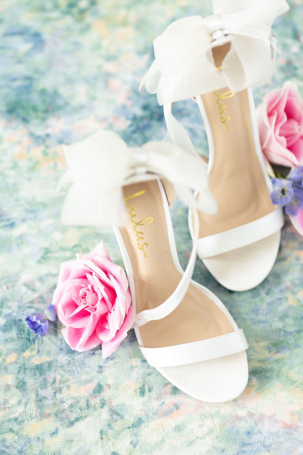 White bridal sandals with bow details and pink roses on watercolor background.