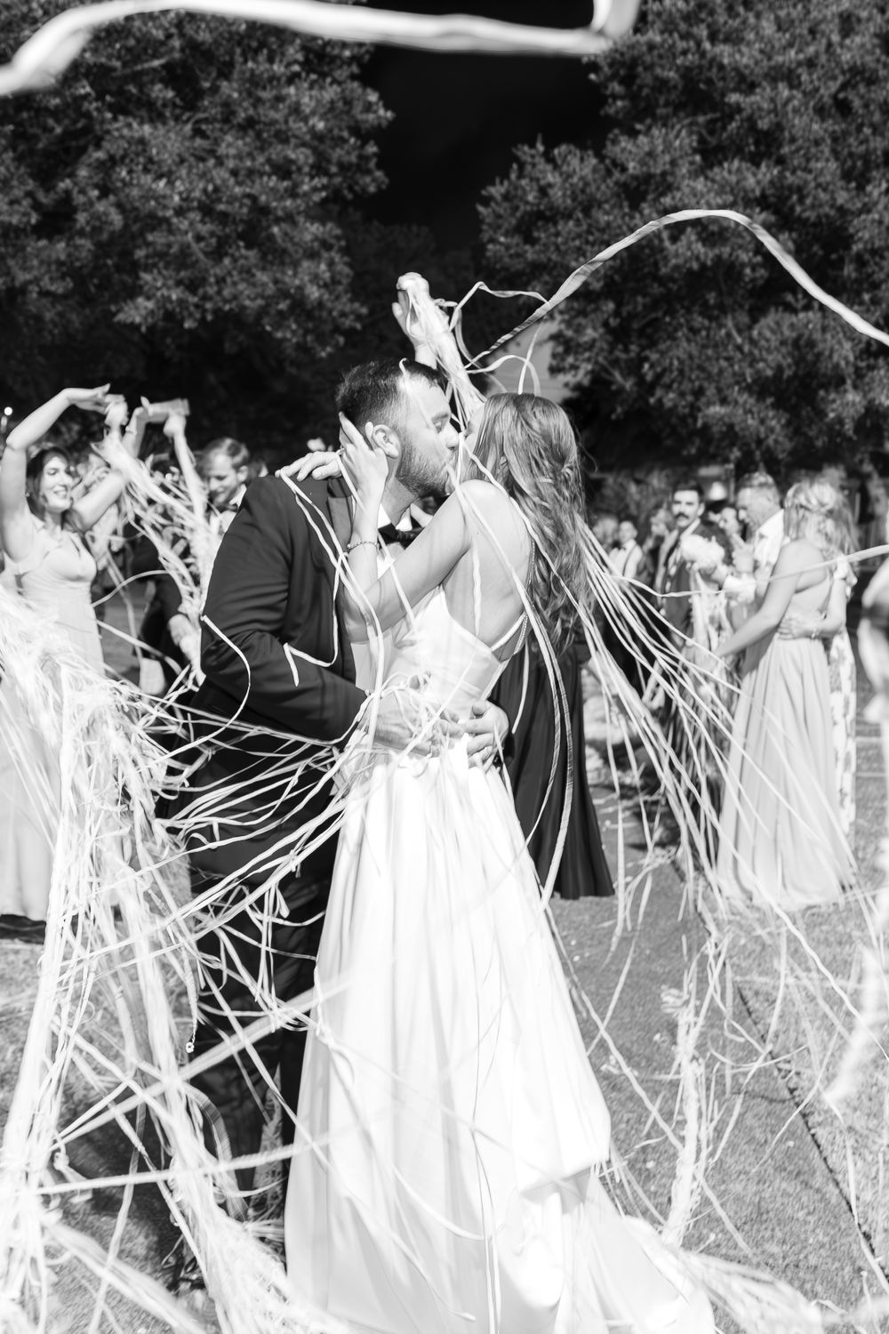 Black and white photo of wedding celebration with guests throwing streamers outdoors.