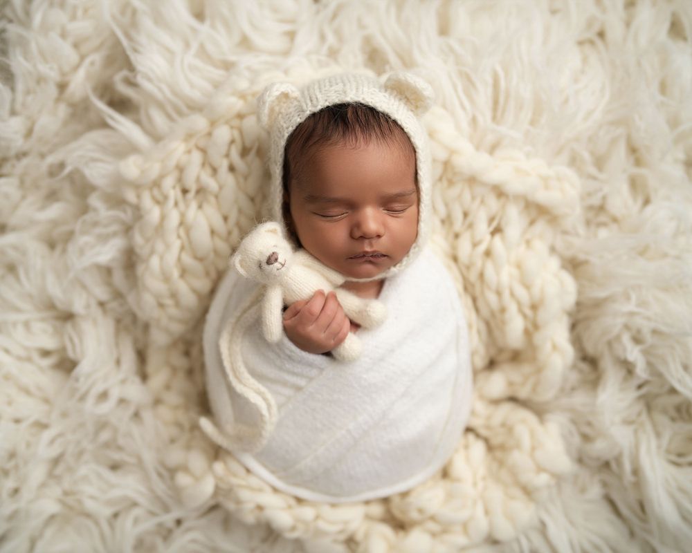 Sleeping newborn wrapped in white swaddle on fluffy cream-colored rug.