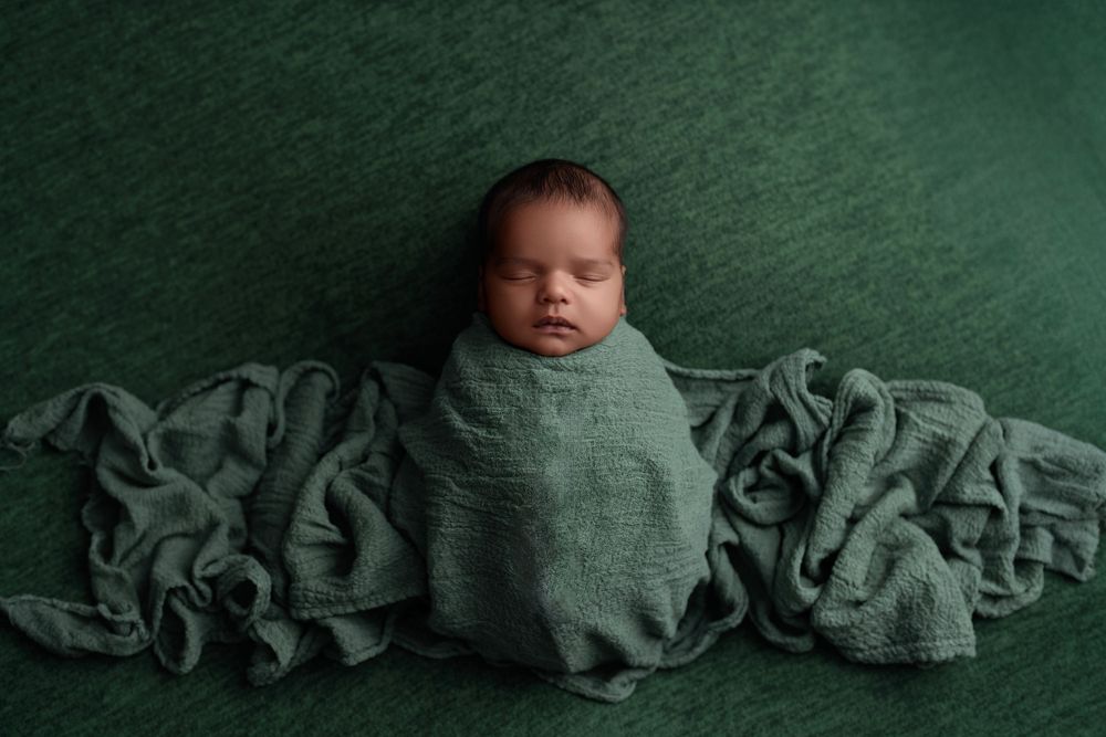 Sleeping newborn baby wrapped in soft green blanket against matching textured green backdrop during photo session.