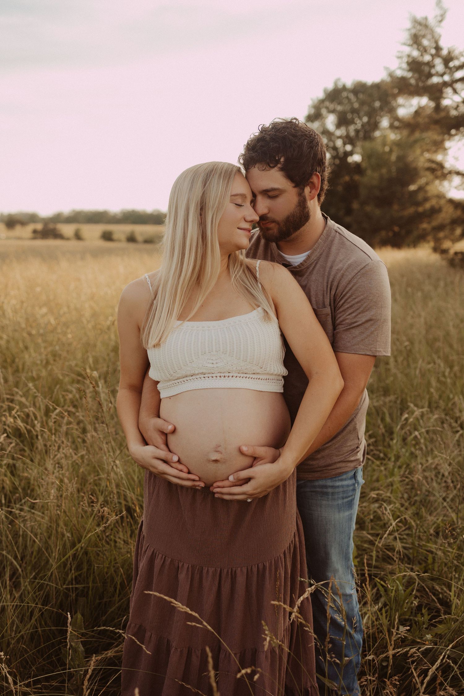 dad cuddles moms exposed belly during maternity session in field