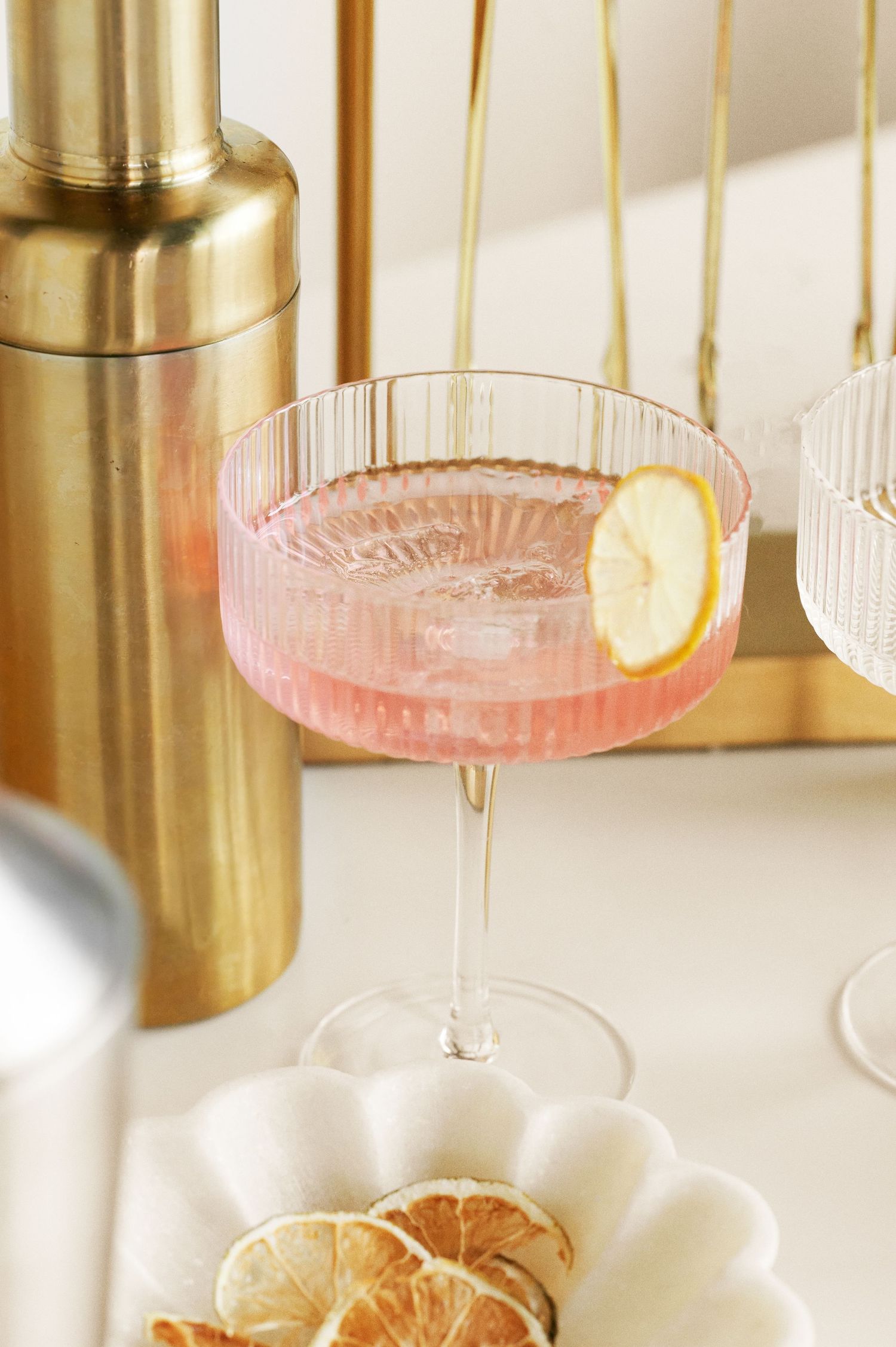 Pink cocktail in vintage coupe glass with citrus garnish and gold bar accessories.