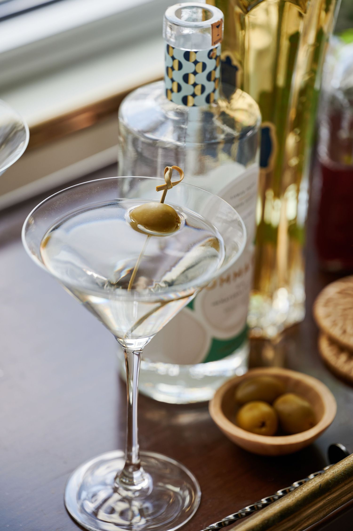 Elegant martini glasses and olives arranged on a bar cart near a window.
