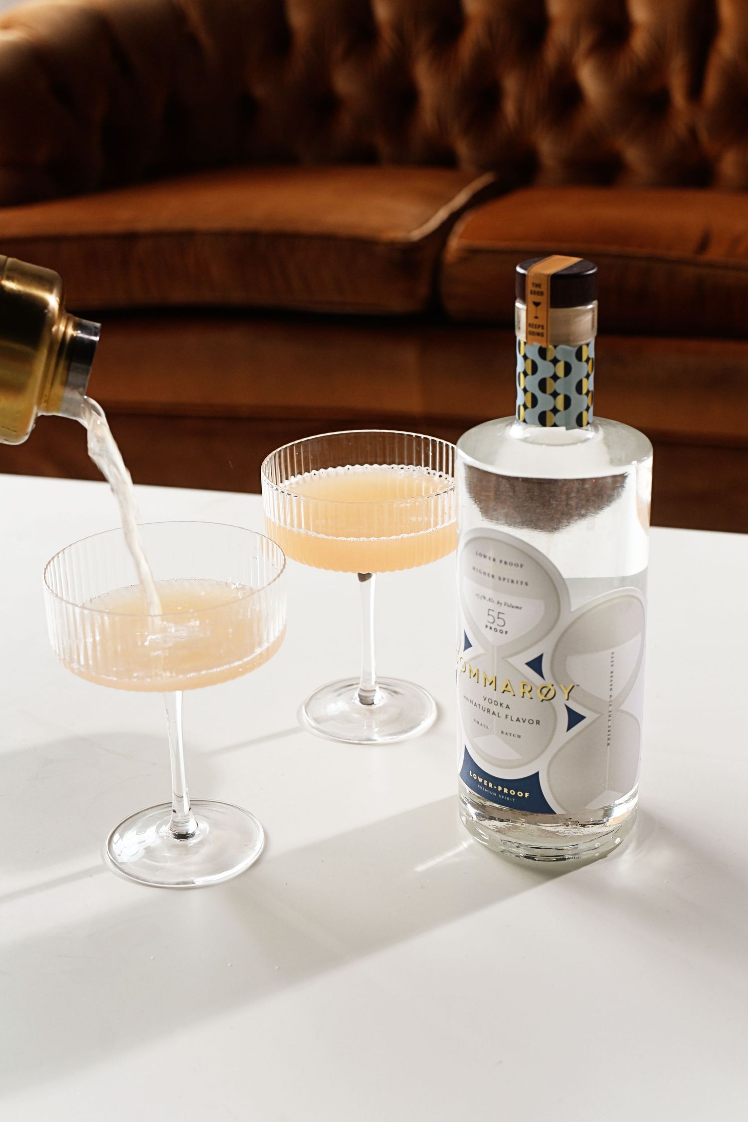 Minimalist arrangement of crystal cocktail glasses and bottles on white surface.