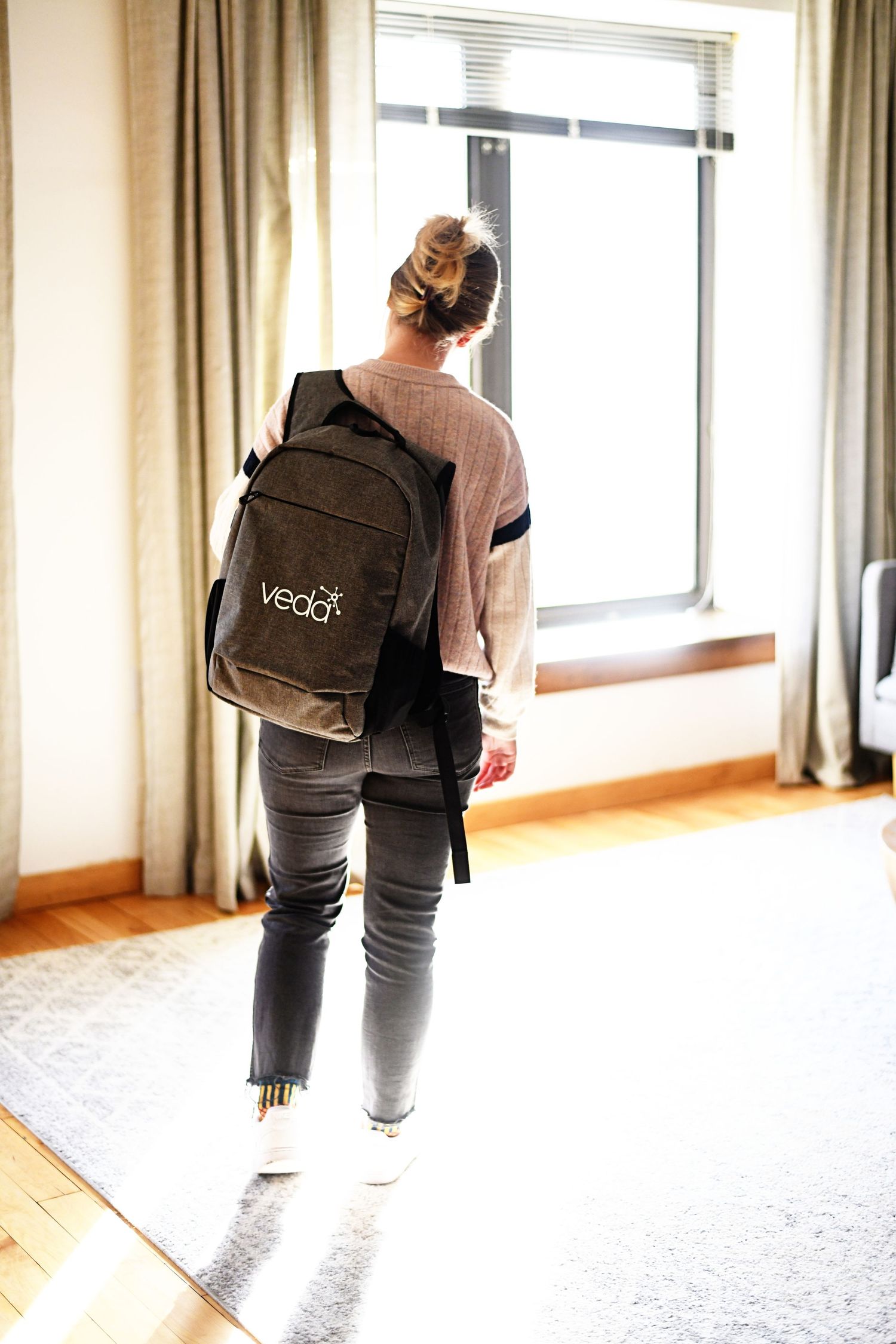Person carrying messenger bag walking through bright office hallway with large windows.