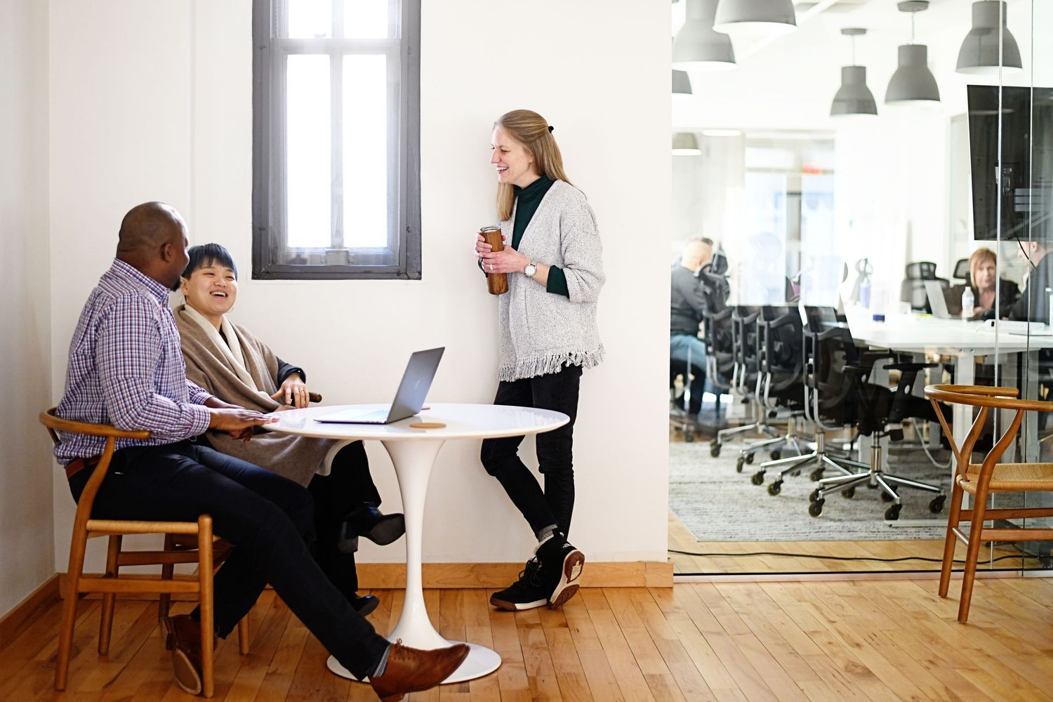 Modern open office workspace with white desks, pendant lighting and people working at tables.