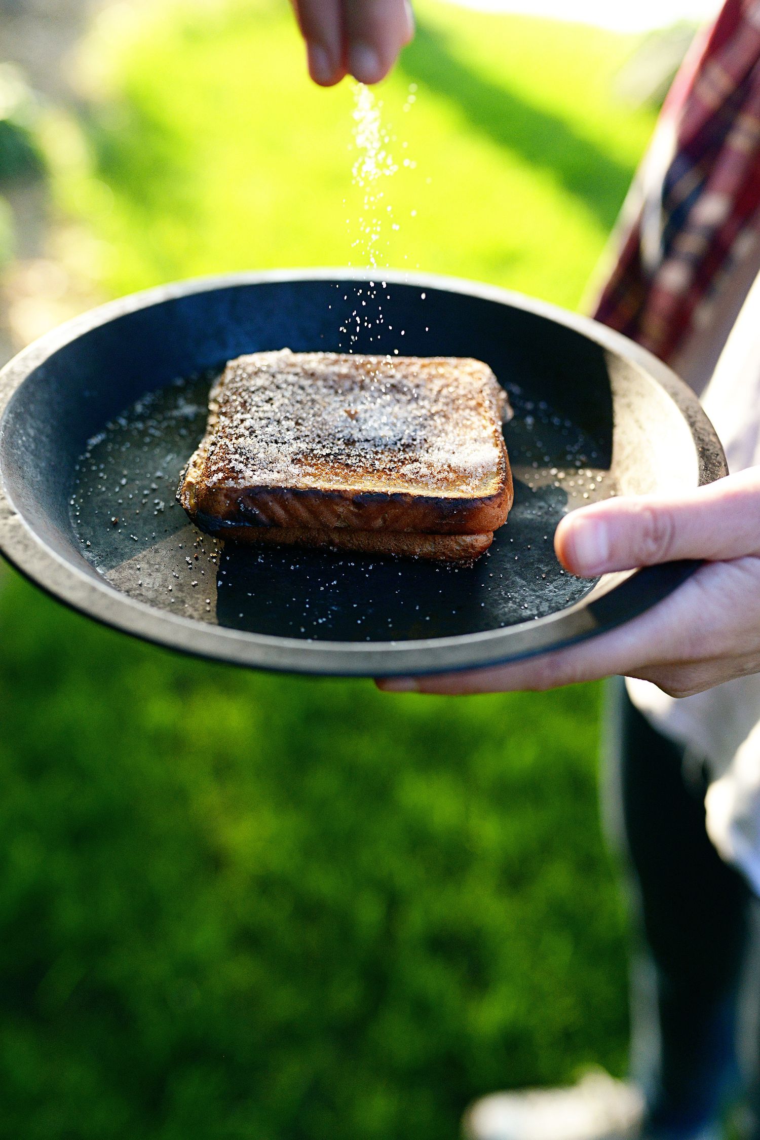 Sequential shots of seasoning being sprinkled onto grilled salmon on a black plate.
