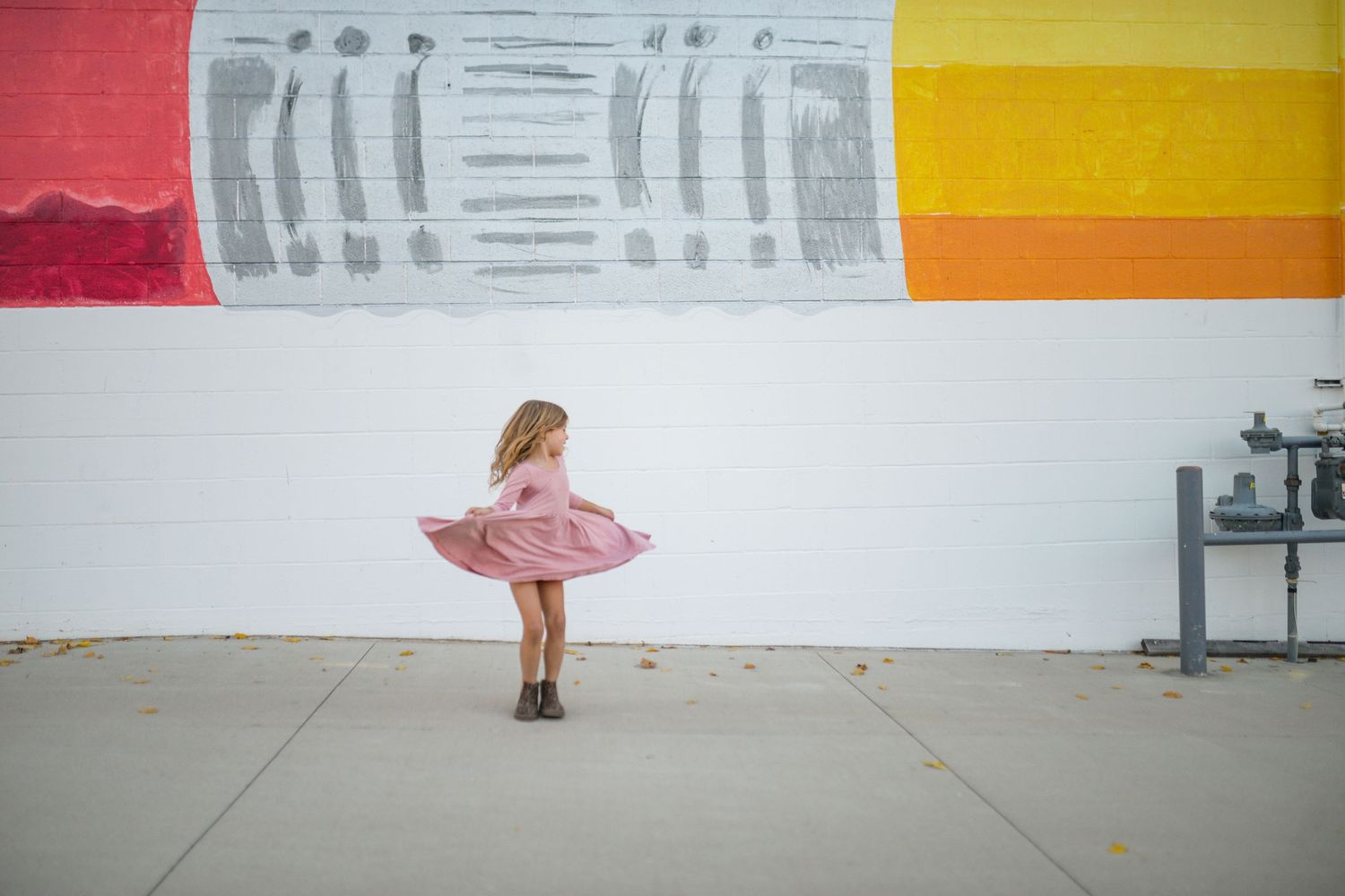 Pink dress twirling against large pencil mural on white wall.