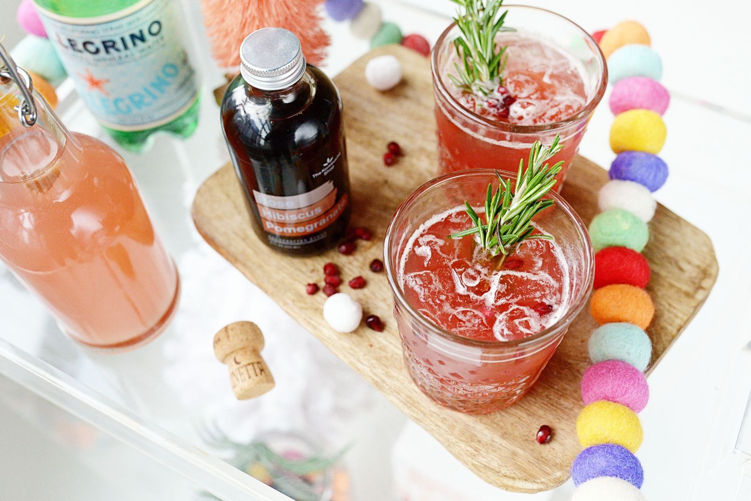 Colorful cocktails garnished with rosemary and fruit on a festive serving board.