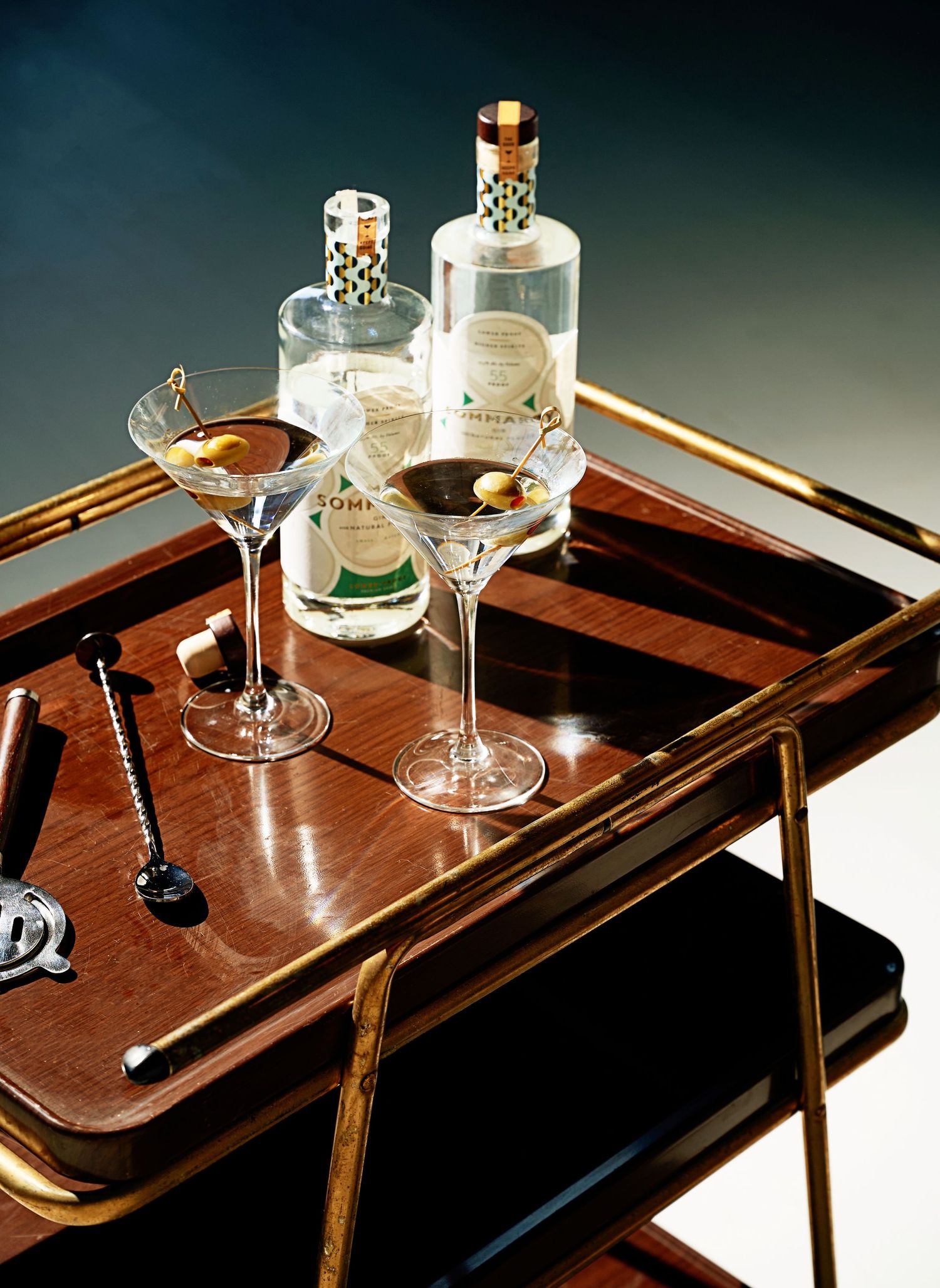 Vintage wooden tray with martini glasses and cocktail accessories in dramatic lighting.